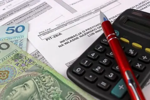 Formularz PIT-28/A, polskie banknoty, kalkulator i długopis.